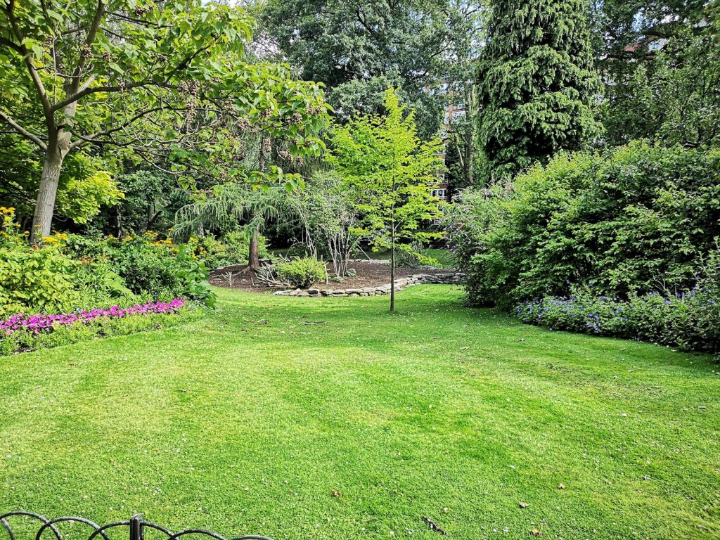 Gepflegter Garten mit Rasenfläche, Beeten und altem Baumbestand