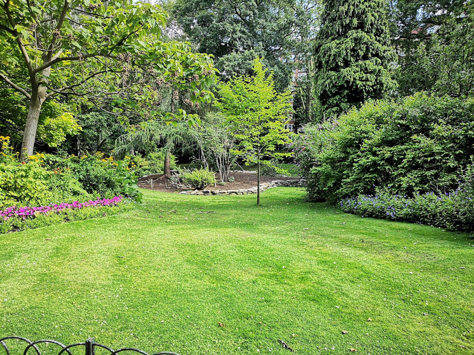Gepflegter Garten mit Rasenfläche, Beeten und altem Baumbestand